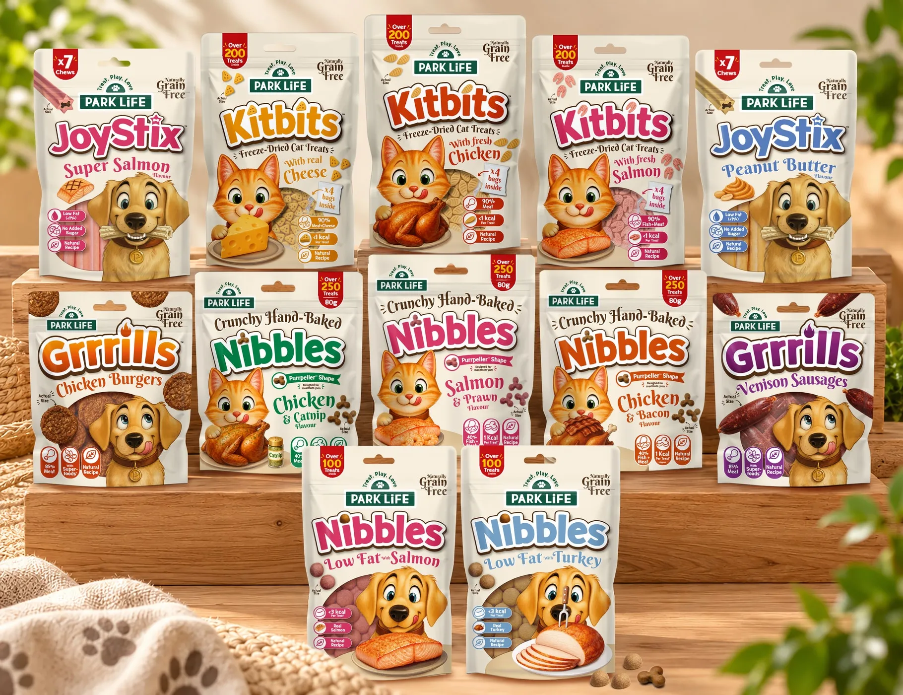 Park Life pet treat pouches on wooden steps: JoyStix chews, Kitbits freeze-dried cat treats, Grrrills, and Crunchy Hand-Baked and Low Fat Nibbles.